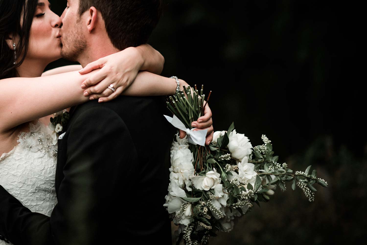 bride and groom embracing and kissing while holding a wedding bouquet overlooking the lake at Hornings Hideout wedding venue in North Plains Oregon by Oregon Wedding Photographer Dionne Kraus